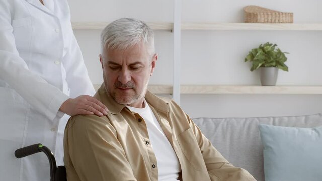 Assistant Touching Disabled Man's Shoulder Supporting Patient During Rehabilitation Indoors