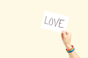 Hand with a rainbow bracelet, LGBT symbol, holding a paper with a message: love
