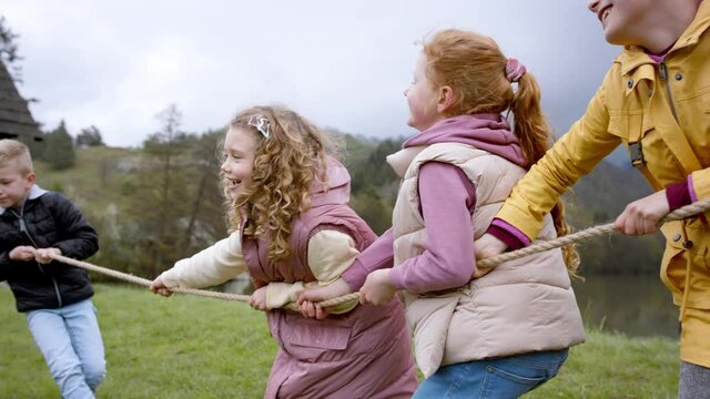 Group of school children and teacher doing rope pulling outside in nature.