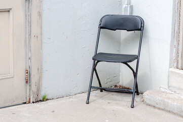 black plastic folding banquet chair opened near the corner of two aged white walls background