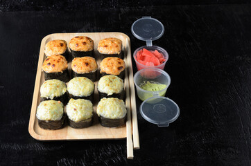 A set of seafood rice rolls wrapped in thin dried sea grass leaves on a wooden platter with ginger and wasabi