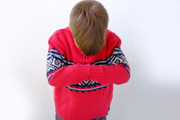offended or punished child, a boy of 7-8 years old in a red Scandinavian sweater bent down on his face, hunched his back, parenting concept - obrazy, fototapety, plakaty