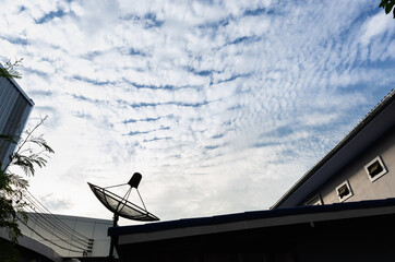 Signal space satellite communication technology. Satellite dish is on the roof silhouette on the roof. Black satellite dish with blue sky texture and cloudy is background.