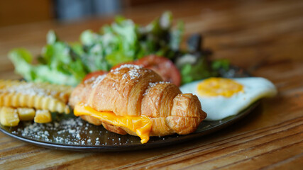 Vegetarian croissant with cheese and porched egg with french fries and vegetable. Healthy European breakfast