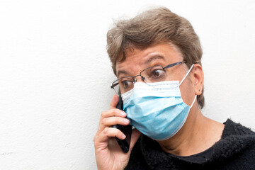 Portrait of an old elder woman with glasses talking on the phone with surprise or scary expression. Scene of COVID or Coronavirus pandemic.