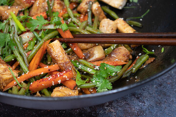 Vegan tofu, beans andcarrot stir fry in black wok, chopsticks, close up