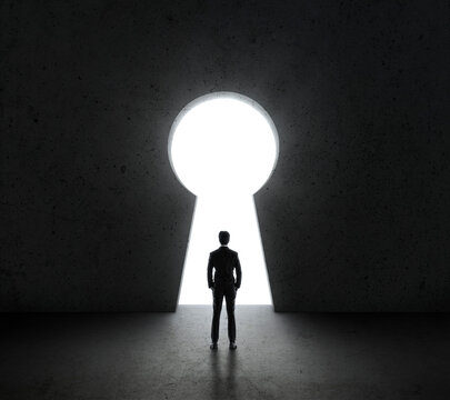 Businessman standing in front of bright big keyhole door