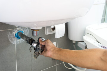 Hand of Plumber holding joints and connections of Basin or sink in a bathroom, Clearing a Clogged Bathroom Sink in a bathroom for unclog a Sink.	