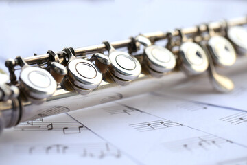 Flute, woodwind brass instrument in classical orchestra. Silver modern flute on white sheet music...