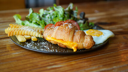Vegetarian croissant with cheese and porched egg with french fries and vegetable. Healthy European breakfast