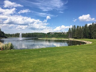A beautiful view of a par 4 golf hole surrounded by a giant lake and a fountain.The scenic hole requires an approach shot over the water and is also surrounded by forest. In Innisfail, Alberta, Canada