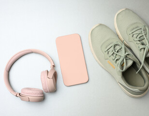pair of pink sneakers, wireless headphones, a smartphone on a gray background.