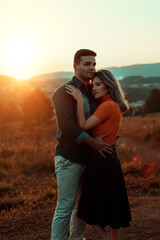 Casal de namorado, ao pôr do sol, abraçados, mulher de blusa laranja e homem de camisa jeans, abraçados olhando para o horizonte.