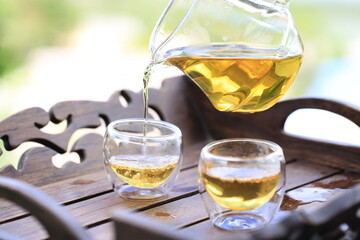 Hot clear tea in transparent jag and glass on table with reflection in nature. Tea set in tea field at Mae Hong Son, Thailand.