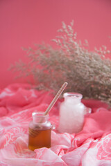 Honey with stick in jar and sugar or sea salt in jar with sweet pink background with flower