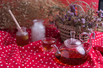 Tea pot and tea cup on wood table with honey and suagr in mag with flower basket on red cloth napkin