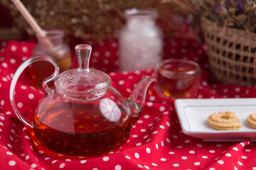 Tea pot and tea cup on wood table with honey and suagr in mag with flower basket on red cloth napkin, with butter cookies and brownies