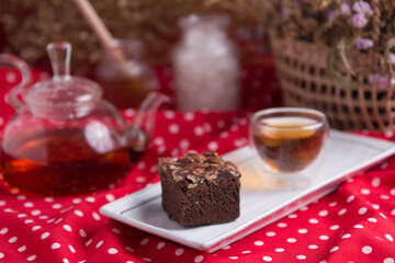 Tea pot and tea cup on wood table with honey and suagr in mag with flower basket on red cloth napkin, with butter cookies and brownies