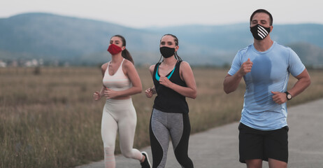 Three multiethnic women runners group wear face masks running keep social distance outdoor. Fit healthy diverse team wear sportswear jogging in park on nature sport track distancing for safety.