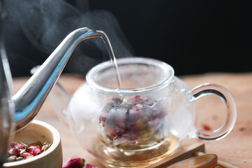 Rose tea with transparent glass and jug with dried rose flower on wood board. Aroma rose hot drink  for healthy  by flower tea.