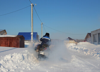 Russia, Novosibirsk 12.02.2021: a man rides a snowmobile with smoke in a village in winter in Siberia