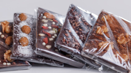 Close up of dark milk chocolate bars with nuts and almonds, on a light gray background.