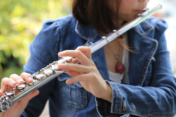 Flute classical instrument player playing song. Instructor practicing bronze woodwind for orchestra as solo with green bokeh outside with nature.