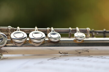 Flute, woodwind brass instrument in classical orchestra. Silver modern flute on white sheet music...