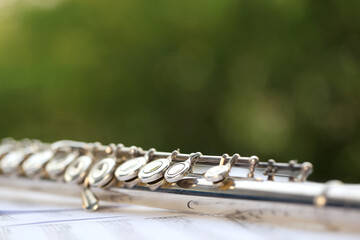 Flute, woodwind brass instrument in classical orchestra. Silver modern flute on white sheet music...