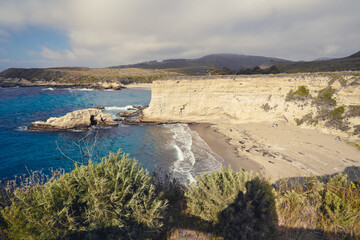 Montana de Oro State Park, California Central Coast. Beautiful sand beach, rocky cliffs, native plants, and cloudy sky on background