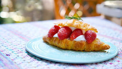 Croissant with strawberry and white softly mousse cream on blue ceramic plate with icing. French dessert assorted red berry.