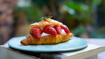 Croissant with strawberry and white softly mousse cream on blue ceramic plate with icing. French dessert assorted red berry.