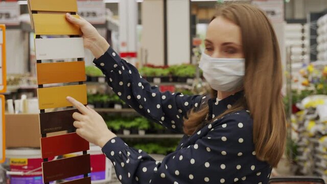 Woman in a protective mask chooses a color of paint for a tree in a hardware store