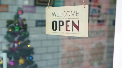 Open and closed flip sign in front of coffee shop and restaurant glass door. Wooden sign with wording of place's status. Say sorry we're closed. Please come back again and another side.
