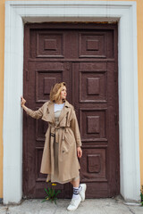 Obraz premium Young millennial woman with wild hair dressed in an autumn coat posing near the door of an old building.