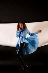 vertical portrait of a curly model wearing a blue dress and black latex pants with black and white paper like background
