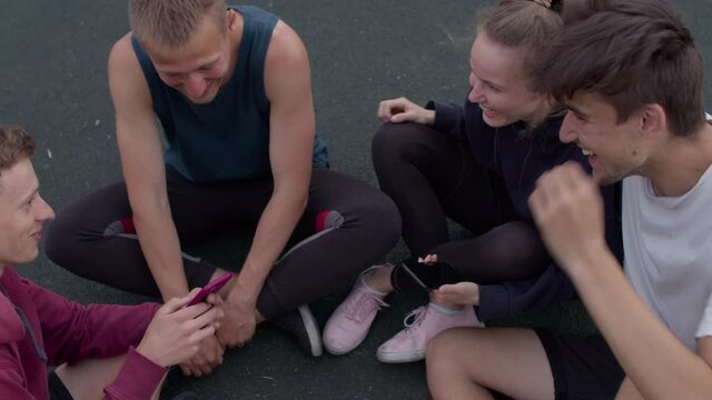 Friends sit on the playground and discuss photos after playing football or playing sports in a sunny day. 4K RAW graded footage