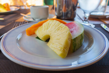 Plate of juicy fruits in outdoor restaurant. Hotel breakfast. Served breakfast table. Slice of pineapple, watermelon and papaya on plate. Delicious dessert. Fresh fruits on table. Fruits and coffee.