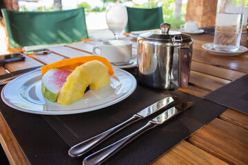 Plate of juicy fruits in outdoor restaurant. Hotel breakfast. Served breakfast table. Slice of pineapple, watermelon and papaya on plate. Delicious dessert. Fresh fruits on table. Fruits and coffee.