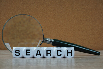 Magnifier and search word written on cube over wooden background. Glossary Concept.