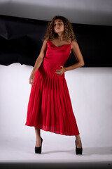 vertical portrait of a latin woman posing and wearing a red elegant dress with black and white paper like background
