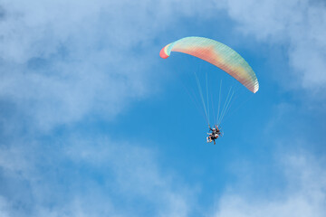 People flying free on a colorful paraglider through the clouds on a blue sky with copy space 