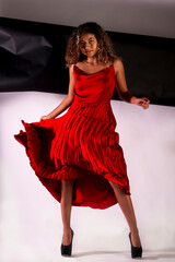 vertical portrait of a latin woman posing and wearing a red elegant dress with black and white paper like background