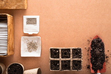 Lettuce seeds and many other vegetable seeds in small envelopes with a shovel and peat pots and trays full of potting soil ready for sowing, on a raw surface with space for text