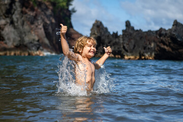 Amazed excited kid in sea water. Funny kid playing on beach.