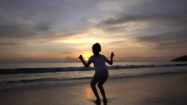 Silhouette Asian teen girl 6 years old standing on beach at sunset raising arms on beach enjoying Amazing sunset or sunrise on summer travel vacation holiday Happiness travel and bliss concept video