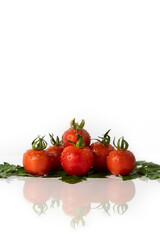 Ripe cherry tomatoes with drops of water and green leaves on a white background with copy space and reflections on the surface.