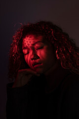 vertical portrait of a young latin woman with red ligth, closed eyes and dark background