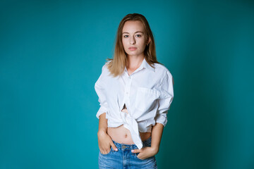 Young blond woman of caucasian ethnicity posing in a white shirt and jeans on a blue background