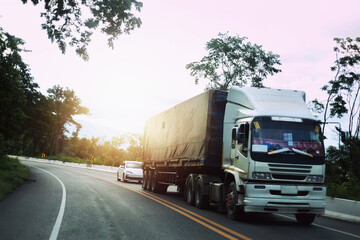 The truck drives on the highway winding through the landscape of the sunset forest.